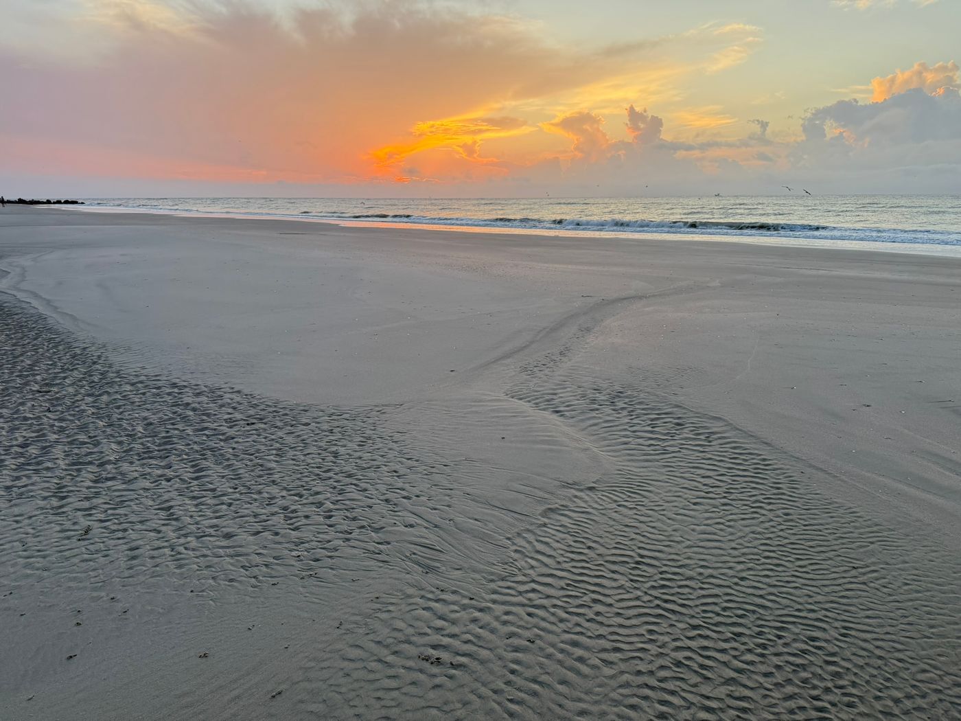 Rippled sand on a wide beach at dusk, with an orange sky over the surf